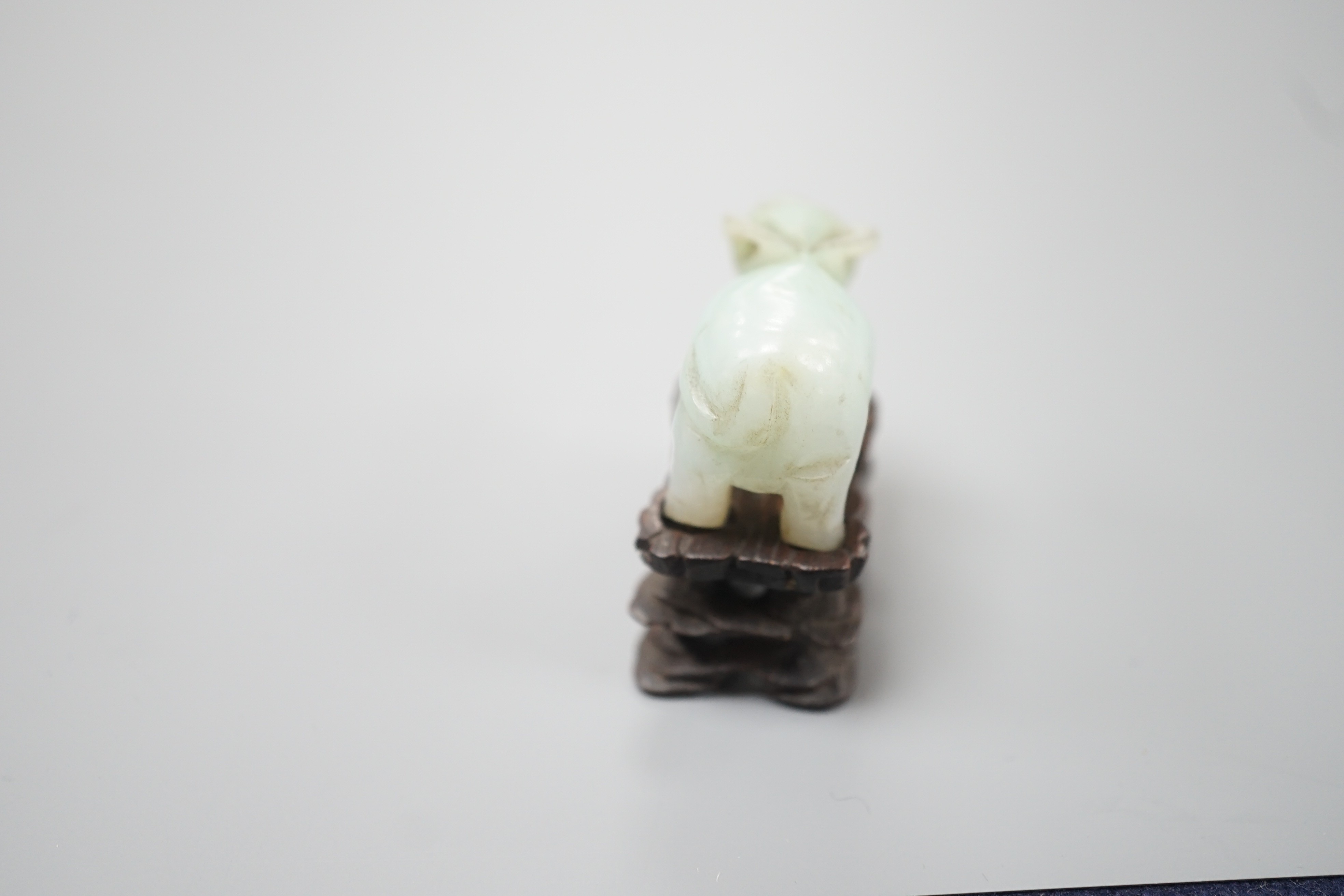 A small Chinese jade figure of a buffalo, late 19th/early 20th century, 3.8cm long, wood stand